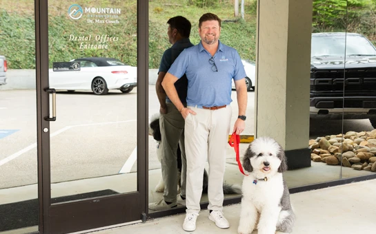 Orthodontist Max Couch, Jr. standing at the front entrance with Pete, the therapy dog